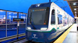 A Sound Transit Link light-rail car numbered 212A displays 'SeaTac Airport' on its destination board as it sits at the SeaTac/Airport station platform at dusk, featuring the agency's blue, white, and teal livery with LED headlights illuminated.