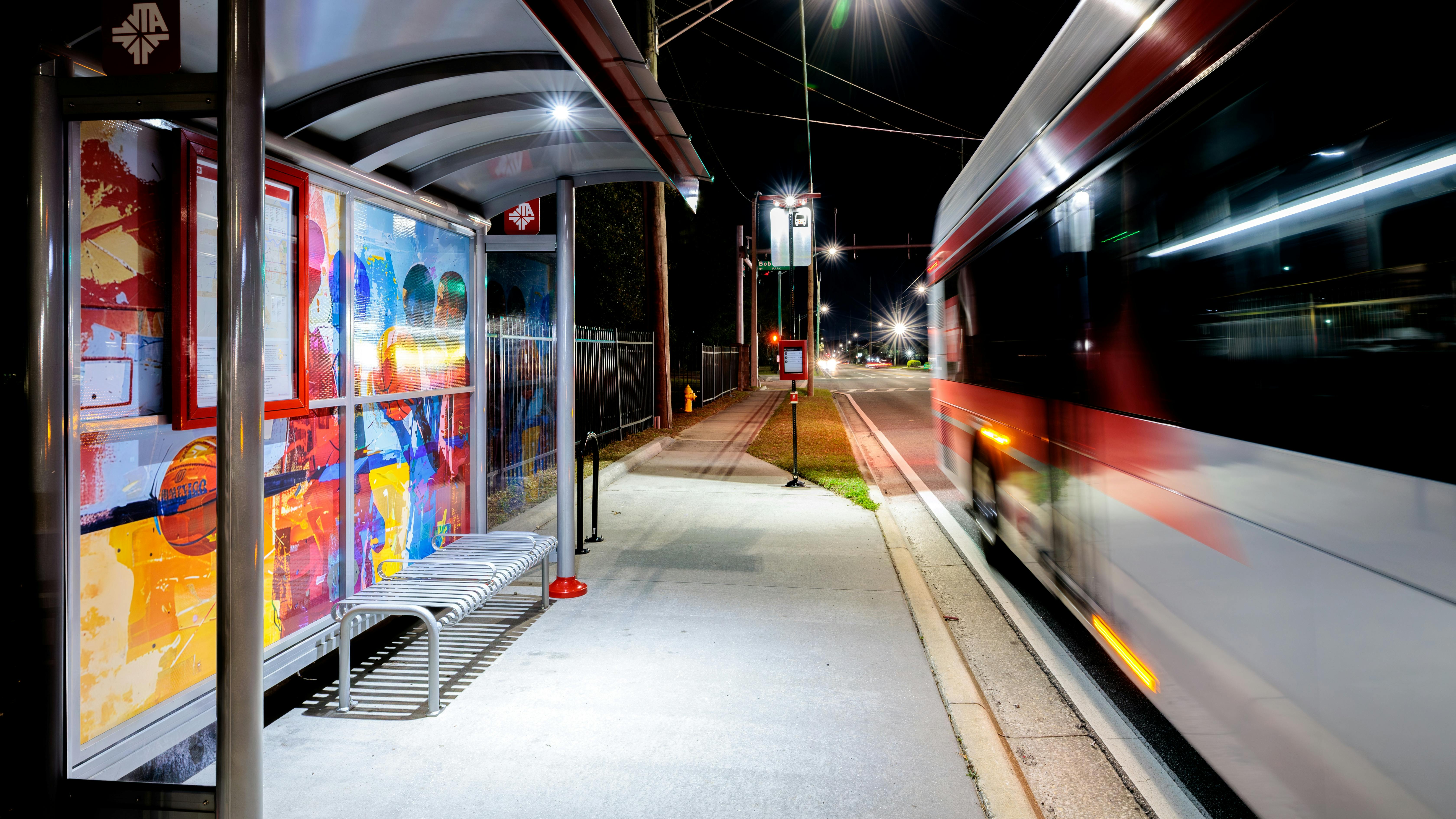 The image displays a lit up bus shelter at night next to an unmarked bus.