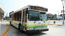 A city of Windsor Transit bus number 444 with a white exterior and green, yellow, and blue horizontal striped livery displays '1A Transway' on its destination board while stopped at a transit terminal, with a front-mounted bicycle rack and ADA accessibility symbol visible.