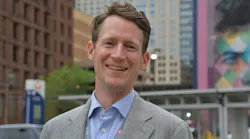 Kyle O'Donnell Burrows stands posed for a headshot wearing a gray suit jacket and blue shirt.