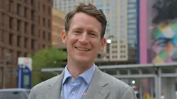 Kyle O'Donnell Burrows stands posed for a headshot wearing a gray suit jacket and blue shirt.