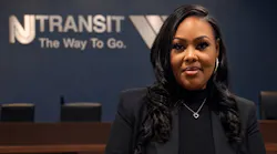Latashia S. Vauss stands in black professional clothing in front of a blurred New Jersey Transit logo.