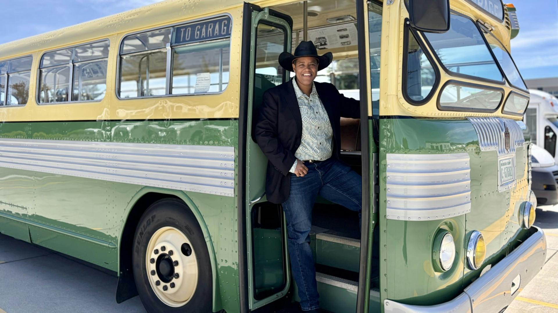 Marah Harris stands in the doorway of a 1948 twin motor coach wearing a black suit jacket and cowboy hat.