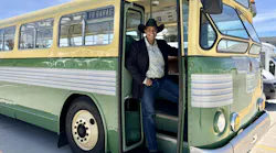 Marah Harris stands in the doorway of a 1948 twin motor coach wearing a black suit jacket and cowboy hat.
