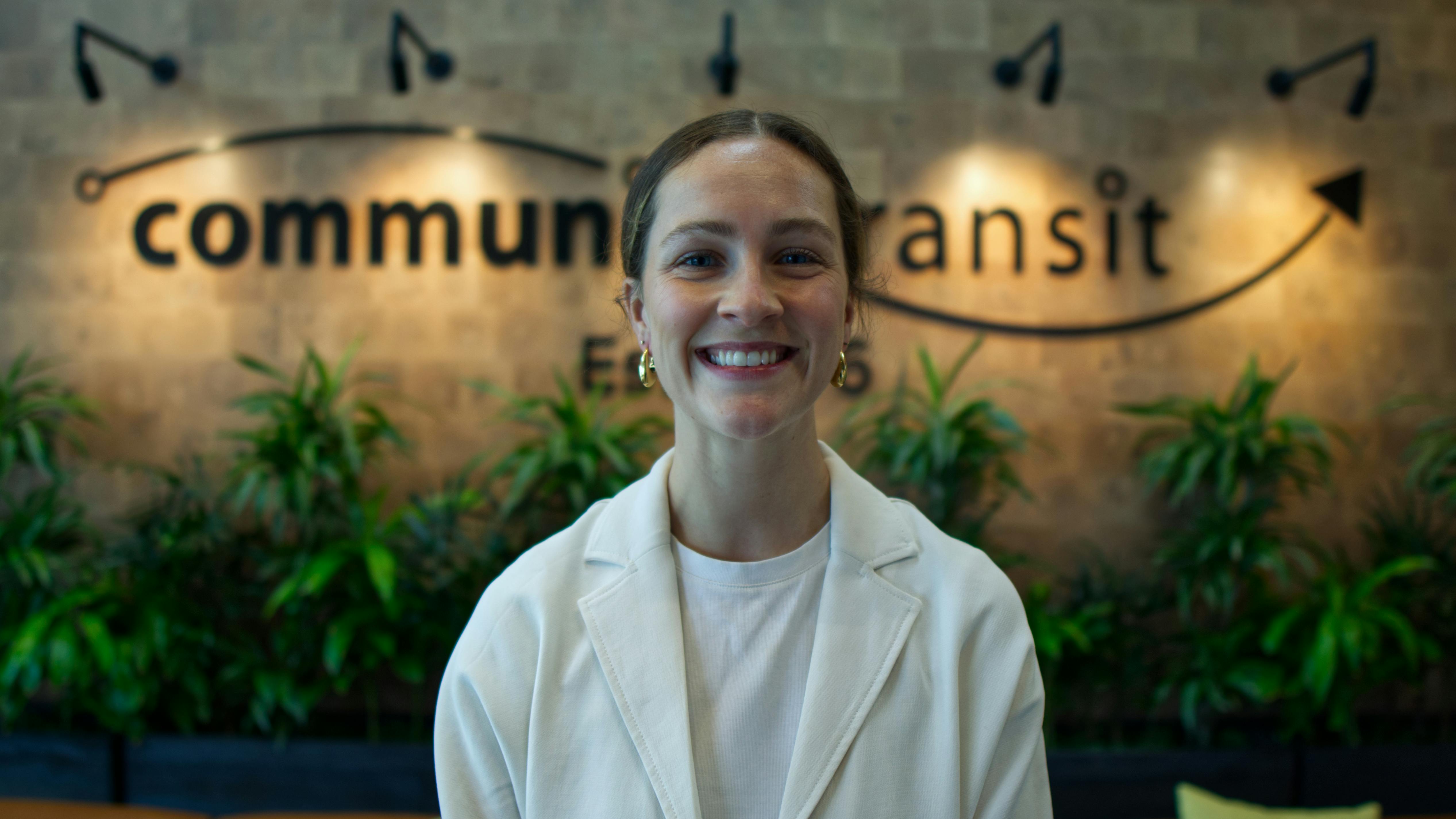 Natalie Lawrence stands smiling in front of a blurred Community Transit logo.