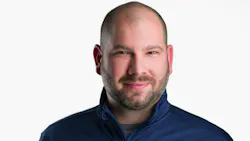 Nickolas Borelli stands in front of a white background wearing a quarter zip.