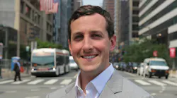 Ryan T. Judge stands in a suit in front of a blurred intersection with a bus in the background.
