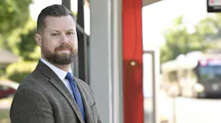 Taylor Eidt stands in front of a blurred bus and bus shelter wearing a suit.