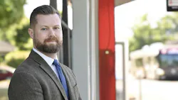 Taylor Eidt stands in front of a blurred bus and bus shelter wearing a suit.