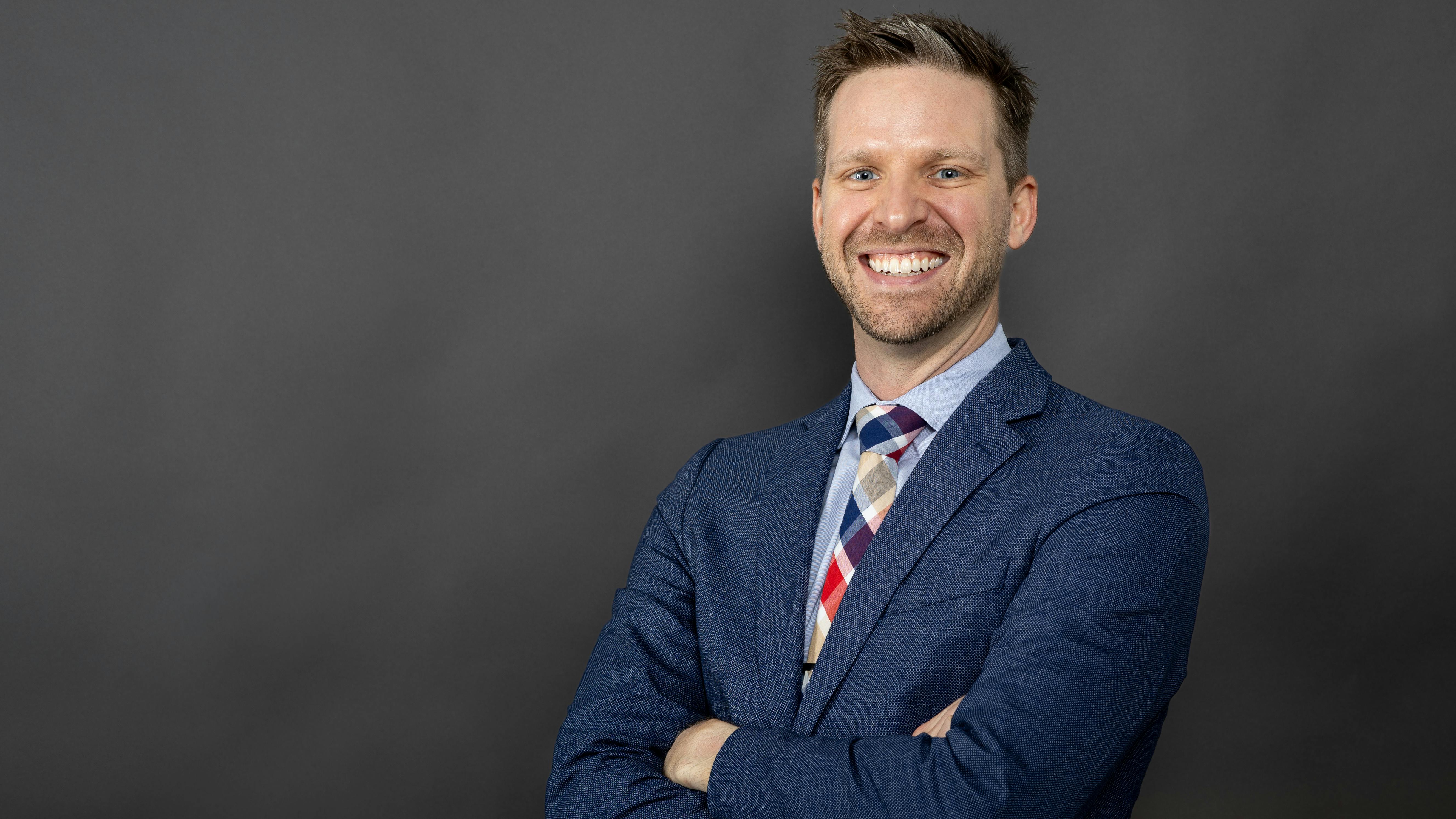 Trey Walker, PE, stands in front of a dark gray background wearing a navy blue suit while smiling.