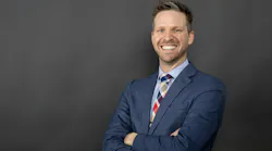 Trey Walker, PE, stands in front of a dark gray background wearing a navy blue suit while smiling.