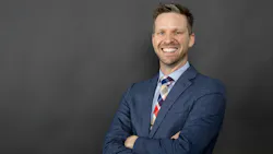 Trey Walker, PE, stands in front of a dark gray background wearing a navy blue suit while smiling.