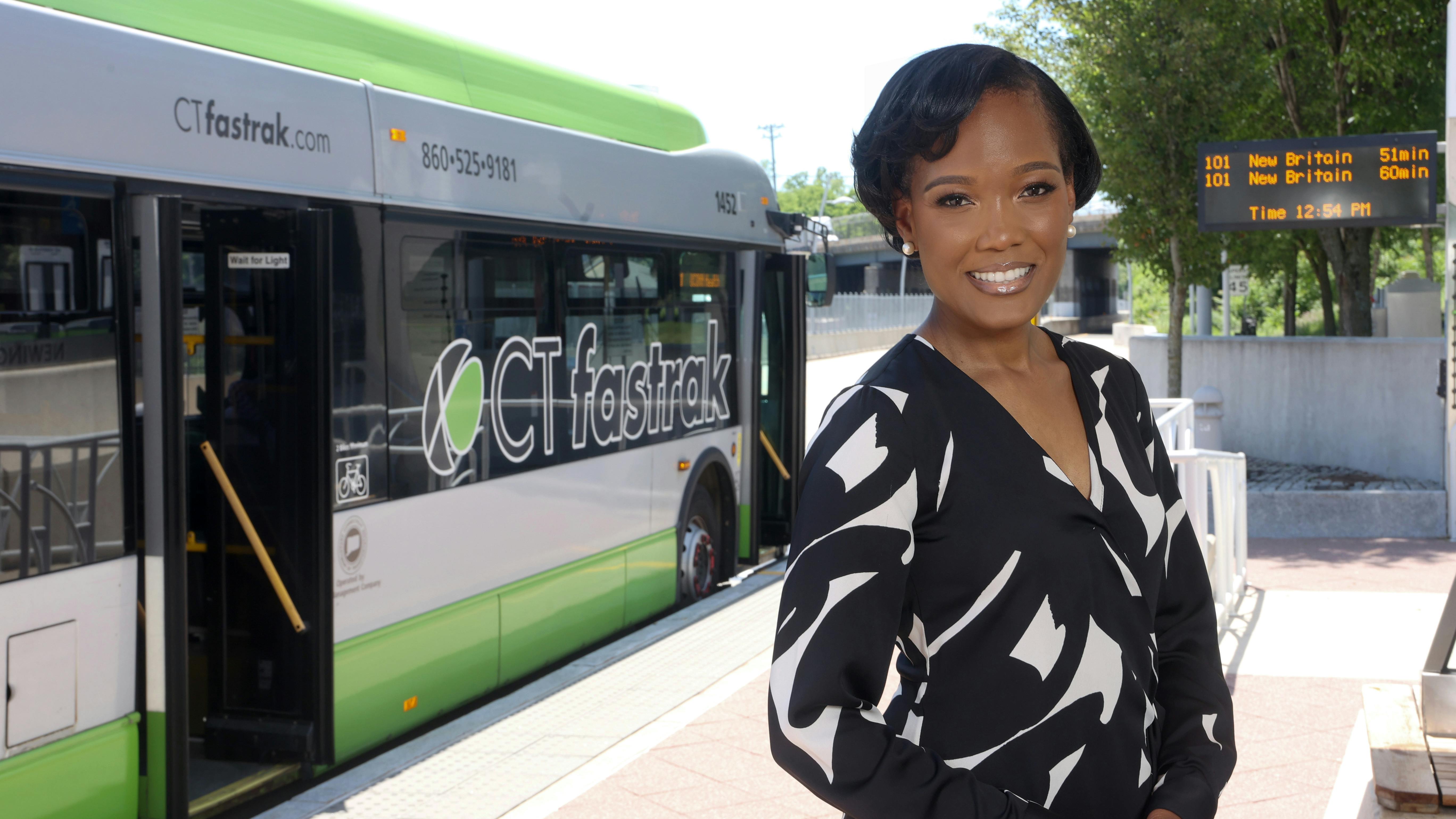 Trish L Chastanet, PMP, stands smiling in a blouse in front of a CT fastrak bus.
