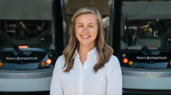 Lauren Krutty, AICP, stands in front of a pair of blurred streetcars. She's smiling and wearing a white blouse.