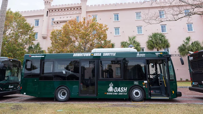A downtown area shuttle sits parked betweeen two other buses.