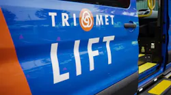 A close-up of a blue and orange TriMet LIFT paratransit vehicle's open side door, with the TriMet logo and 'LIFT' service name displayed prominently and a yellow grab bar and boarding step visible inside.