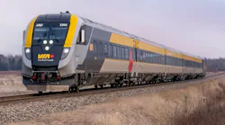 VIA Rail Canada Siemens Venture trainset number 2302 in the agency's gray and yellow livery with a Canadian maple leaf accent, traveling along a rural track through a winter landscape of dormant brush and overcast skies.