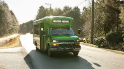 BC Transit small green Chevrolet cutaway bus number 2900 displaying 'Welcome Aboard' on its destination board travels along a narrow, sunlit rural road lined with evergreen trees in British Columbia.