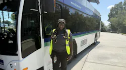 WeDriveU bus operator Charlene Miller stands smiling in a yellow safety vest beside a Concord Kannapolis Area Transit (CK Rider) electric bus displaying the agency's 'Connecting Community' branding and ckrider.com website on a sunny day.