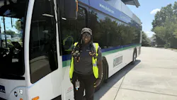 WeDriveU bus operator Charlene Miller stands smiling in a yellow safety vest beside a Concord Kannapolis Area Transit (CK Rider) electric bus displaying the agency's 'Connecting Community' branding and ckrider.com website on a sunny day.