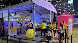 A Brightline branded experiential marketing tent at a FIFA World Cup 2026 fan event in Miami, featuring an 'Explore Florida by Train' display listing stations from Miami to Orlando, a large yellow Brightline-branded soccer ball, and soccer fans in national team jerseys engaging with staff at night.
