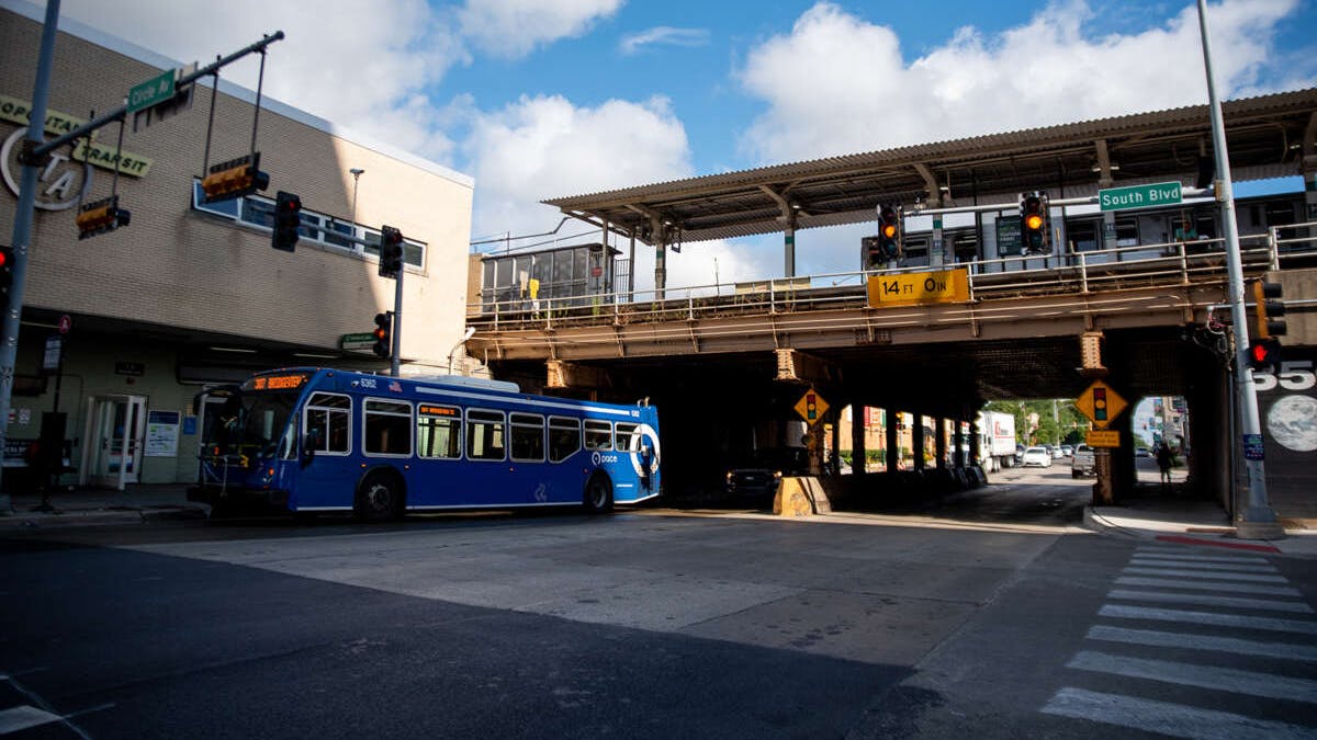 A blue Pace suburban bus stops beneath an elevated CTA rail line at the intersection of South Boulevard and Circle Avenue in Oak Park, Ill., with a '14 FT 0 IN' clearance sign visible under the bridge and traffic signals overhead.