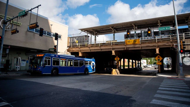 A blue Pace suburban bus stops beneath an elevated CTA rail line at the intersection of South Boulevard and Circle Avenue in Oak Park, Ill., with a '14 FT 0 IN' clearance sign visible under the bridge and traffic signals overhead.