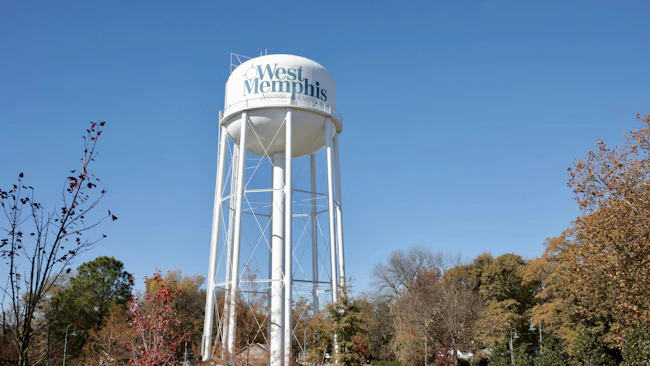 The West Memphis, Arkansas water tower rises above a tree-lined park on a clear autumn day, bearing the city name prominently on its white spherical tank