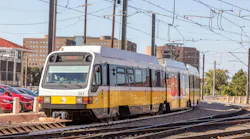 A DART light rail vehicle, numbered 263, rounds a curve on outdoor tracks near overhead catenary wires, with parked cars and mid-rise buildings visible in the background.