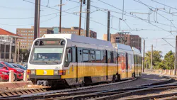 A DART light rail vehicle, numbered 263, rounds a curve on outdoor tracks near overhead catenary wires, with parked cars and mid-rise buildings visible in the background.