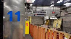 The interior of SEPTA's 11th Street Station on the Market-Frankford Line during a closure for renovation work, showing orange construction fencing, stacked building materials, ladders, exposed masonry walls, and a digital sign reading '11th St Station — L Market-Frankford Line' with an exit sign directing passengers toward 12th & Market Street.