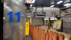 The interior of SEPTA's 11th Street Station on the Market-Frankford Line during a closure for renovation work, showing orange construction fencing, stacked building materials, ladders, exposed masonry walls, and a digital sign reading '11th St Station — L Market-Frankford Line' with an exit sign directing passengers toward 12th & Market Street.