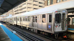 A CTA 'L' train, car 5156, displaying a 'Cottage Grove' destination sign, stopped at an elevated Chicago platform with the agency's blue circular logo on the front car, mid-rise buildings visible in the background.