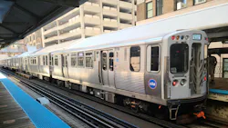 A CTA 'L' train, car 5156, displaying a 'Cottage Grove' destination sign, stopped at an elevated Chicago platform with the agency's blue circular logo on the front car, mid-rise buildings visible in the background.