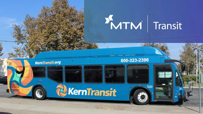 A blue Kern Transit bus parked on a street, featuring a colorful abstract wrap design, the agency's logo and website, and a promotional MTM Transit banner overlaid in the upper right corner.
