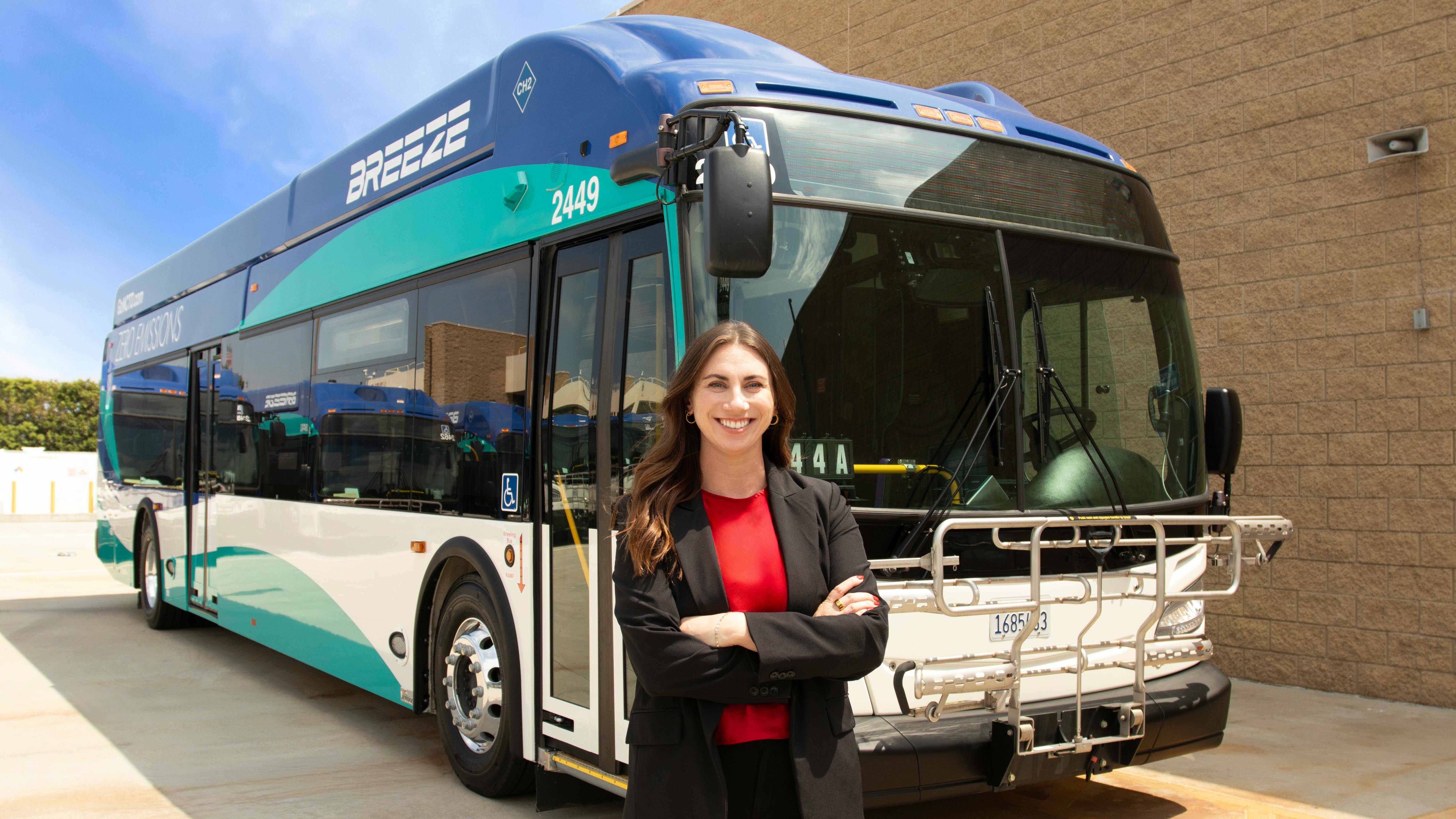 Mary Dover stands smiling in front of a Breeze bus with her arms crossed.