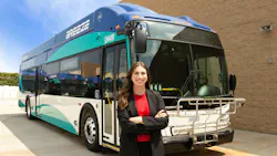 Mary Dover stands smiling in front of a Breeze bus with her arms crossed.
