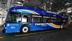 MTA New York City Bus electric bus number 5012 in a deep blue and gold wave livery with 'Electric Bus — Clean-Energy Bus' and 'I ❤ NY' branding displayed inside a bus depot, with charging infrastructure and industrial ceiling systems visible in the background.