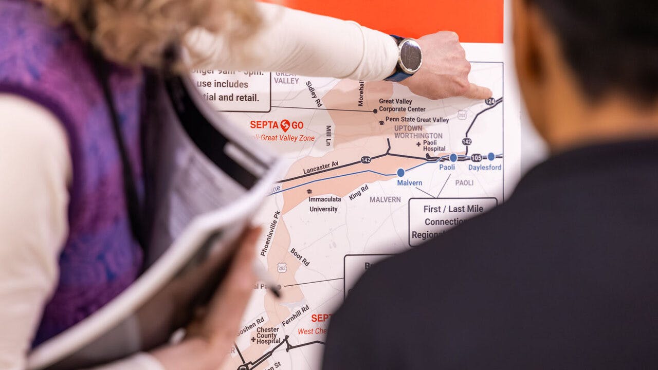 Close-up of two people examining a SEPTA route map showing the Malvern-Great Valley Zone and surrounding communities, with one person pointing to a location near Great Valley Corporate Center.