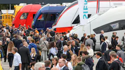 people walk past light rail vehicles at the outdoor display