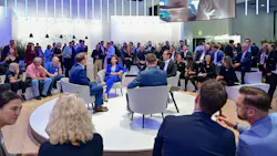 four panelists sit in a circle on a raised circular platform with a crowd around them