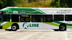 RIPTA R Line electric bus number 2201 in a green and white livery with 'I'm Electric!' branding passes by in motion, displaying 'Training Bus' on its destination board.