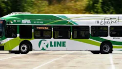 RIPTA R Line electric bus number 2201 in a green and white livery with 'I'm Electric!' branding passes by in motion, displaying 'Training Bus' on its destination board.