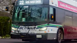 BC Transit CNG bus number 1249 displaying Route 22 Via Hastings on its destination board travels along a tree-lined road in Victoria, B.C., with a front-mounted bicycle rack and a pink university advertisement wrap visible on the side.