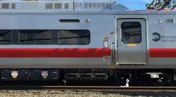 Close-up side view of an MTA Metro-North Railroad train car with its silver, red, and gray livery, showing the entry door, undercarriage equipment, and overhead catenary wires, with a stone platform edge in the foreground.