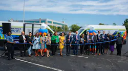A large group of officials and Metro staff cut a ribbon in front of two 'Metro Now' microtransit vans wrapped in the service's branding, celebrating the launch of the Bond Hill-Roselawn service in a parking lot.