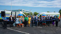 A large group of officials and Metro staff cut a ribbon in front of two 'Metro Now' microtransit vans wrapped in the service's branding, celebrating the launch of the Bond Hill-Roselawn service in a parking lot.