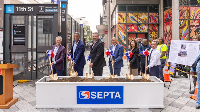 SEPTA officials pose with gold ceremonial shovels at a groundbreaking event for ADA improvements at the 11th Street 'L' station, standing behind a soil-filled planter bearing the SEPTA logo with the station entrance and a colorful mural in the background.
