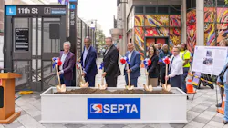 SEPTA officials pose with gold ceremonial shovels at a groundbreaking event for ADA improvements at the 11th Street 'L' station, standing behind a soil-filled planter bearing the SEPTA logo with the station entrance and a colorful mural in the background.