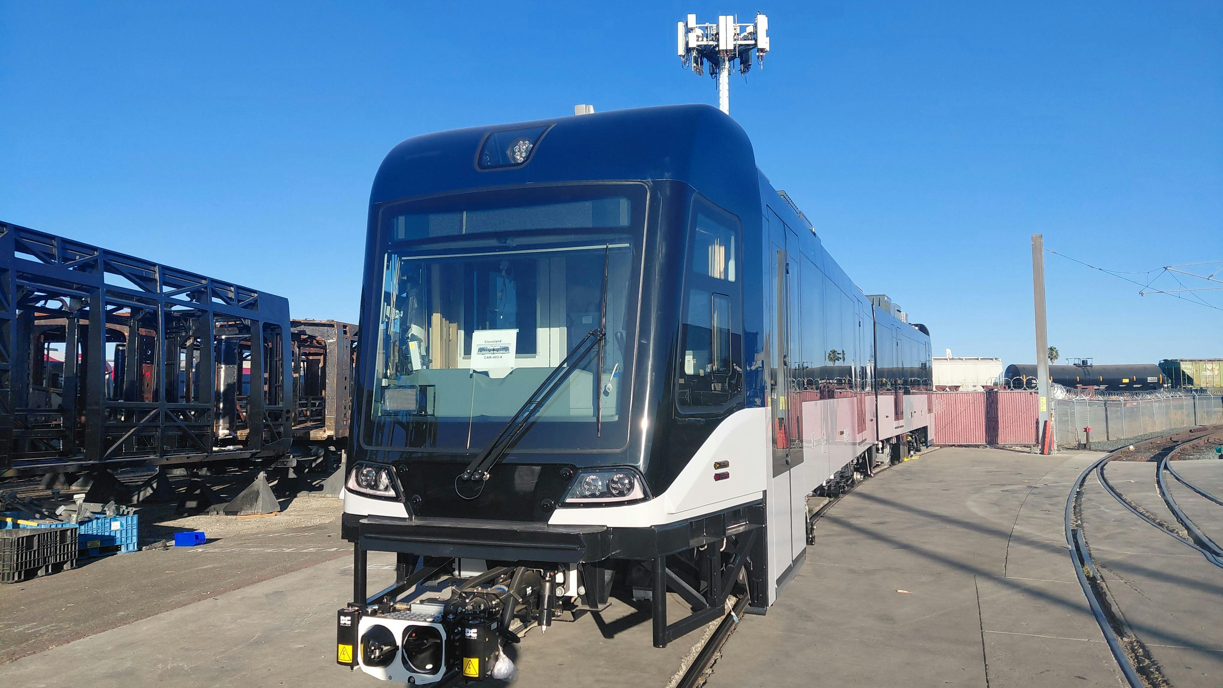 A new Siemens Mobility light-rail vehicle for the Greater Cleveland Regional Transit Authority (GCRTA) sits on a rail yard track under a clear blue sky, featuring a sleek black and white exterior with a modern cab design and roof-mounted equipment, surrounded by industrial yard infrastructure.